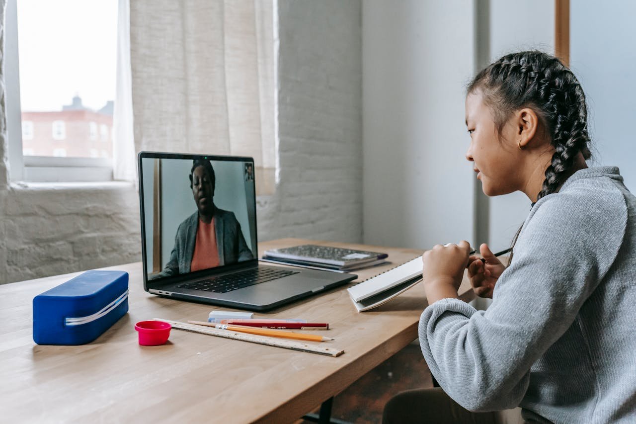 A young girl engages in online education with a teacher via video call, focusing attentively.